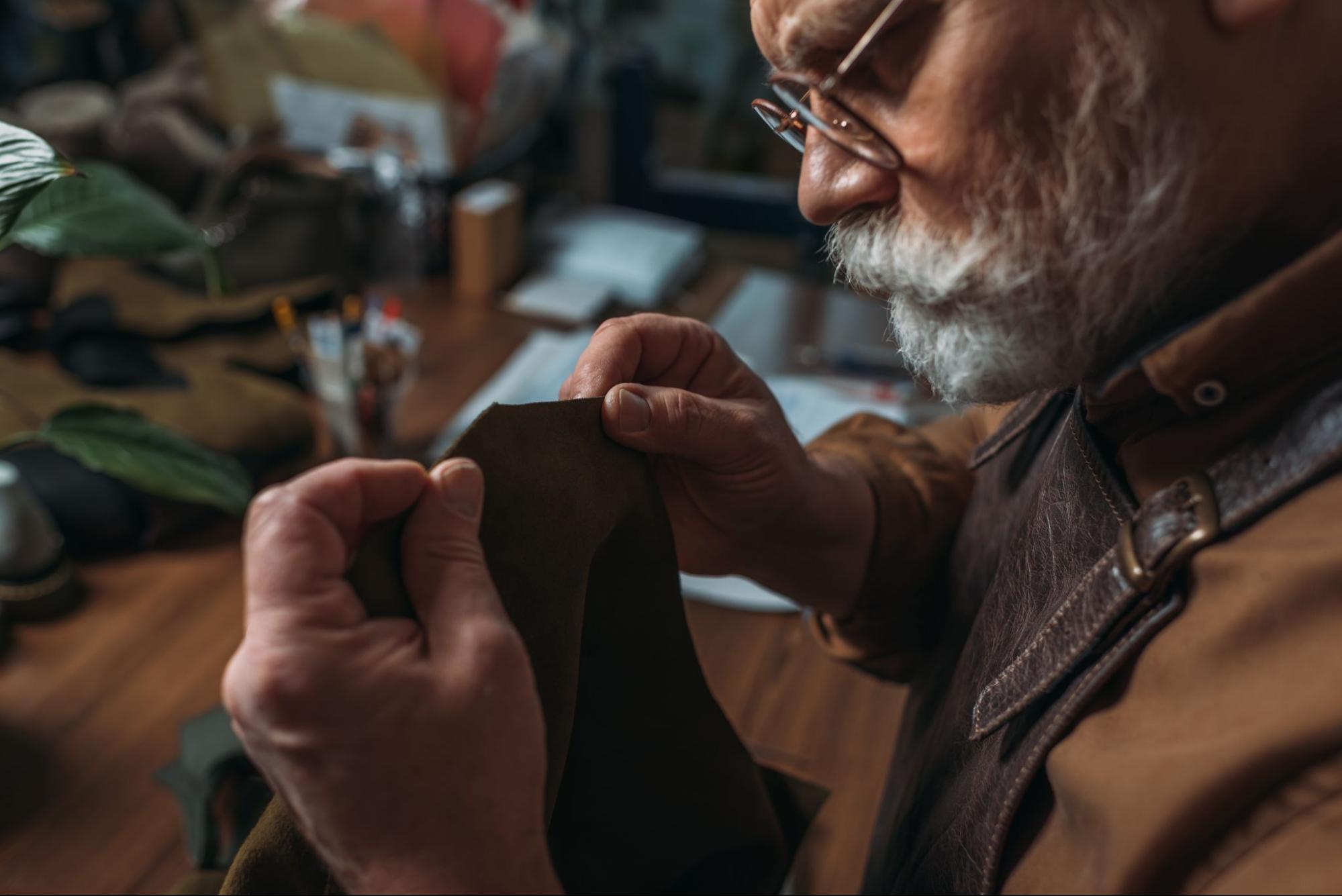 Elderly craftsman sewing brown fabric with focus