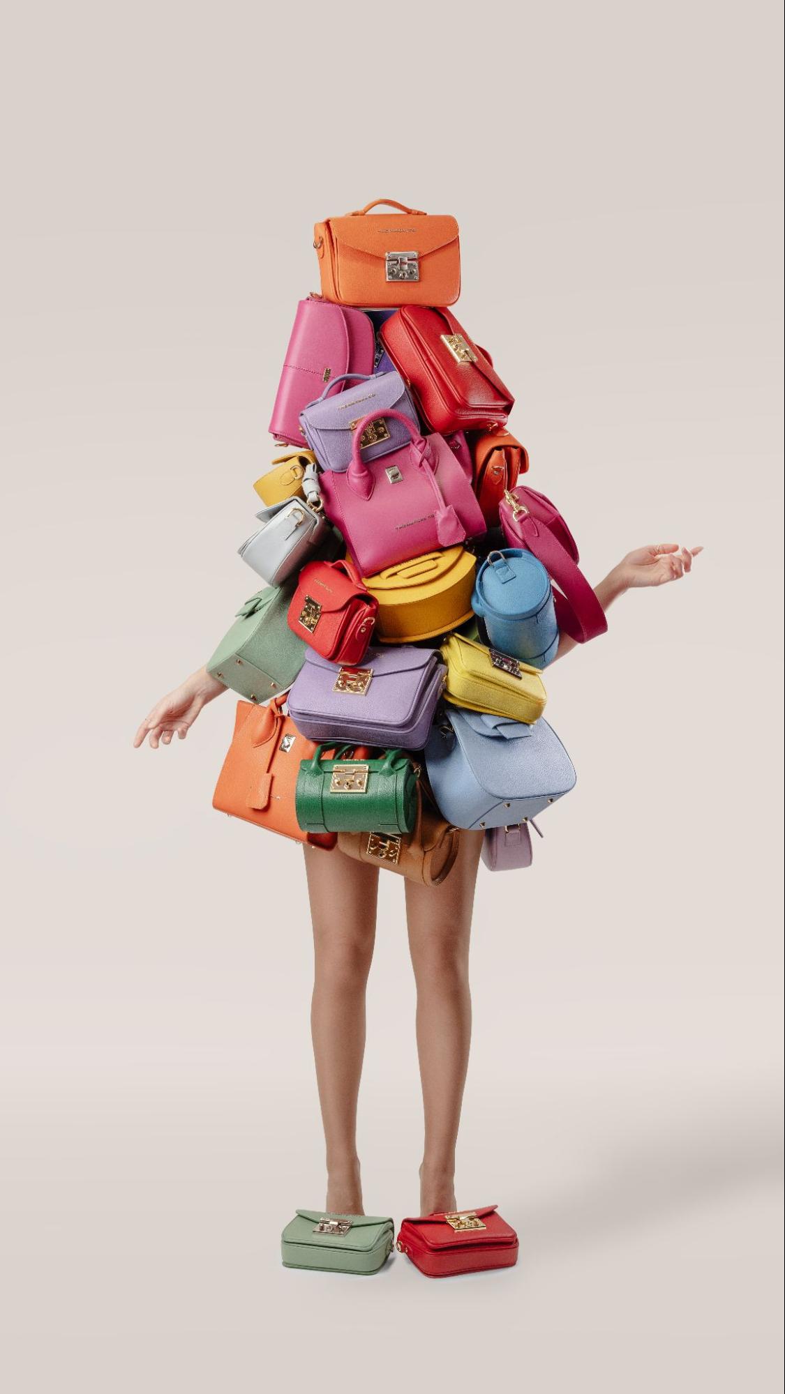 Person covered in colorful handbags stack, showing arms and legs, playful vibe
