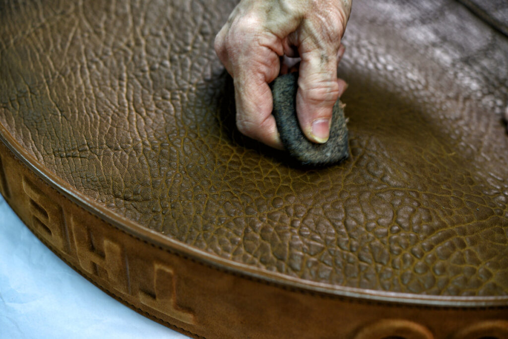 Ruka polira reljefnu braon kožu krpom, ističe teksturu i zanat