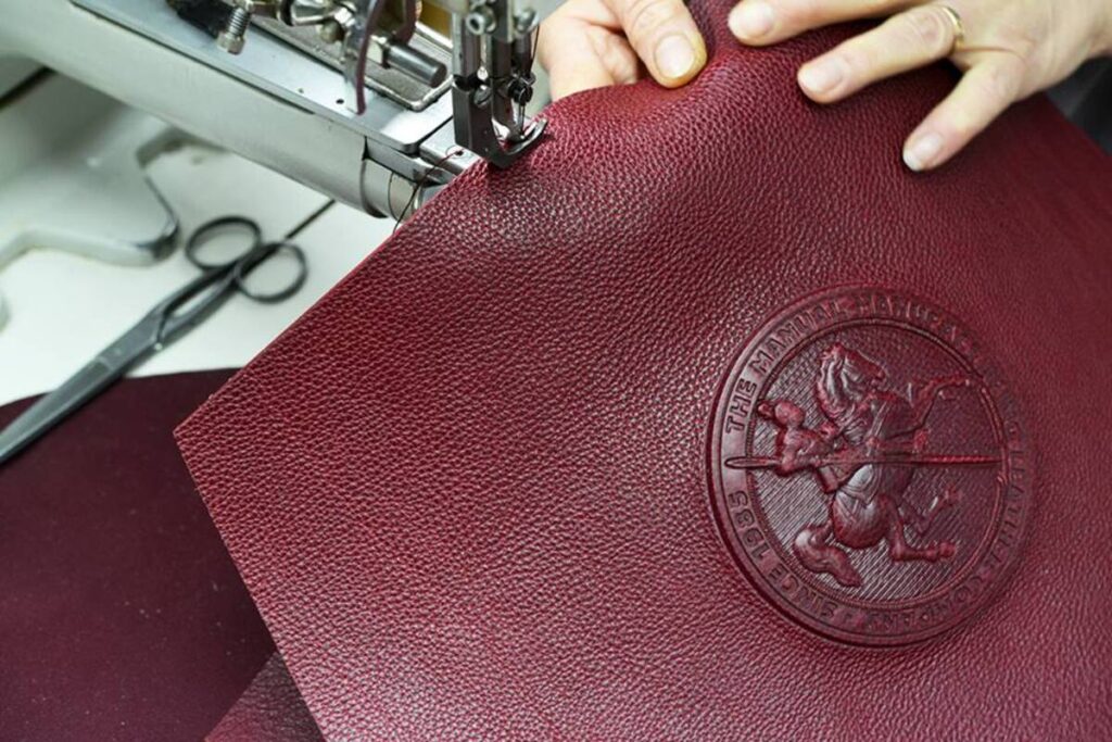 Ruke vode bordo kožu sa utisnutim logom konja kroz šivaću mašinu